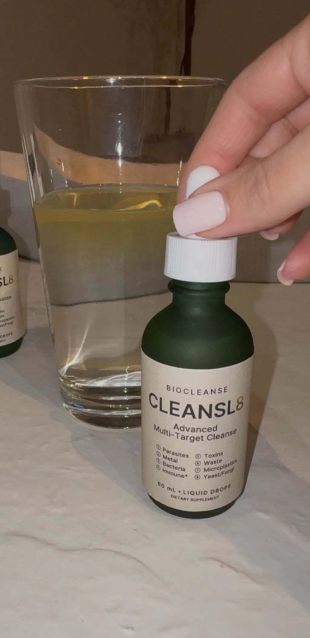 Her hand on the dropper of a CLEANSL8 bottle next to a glass of water
