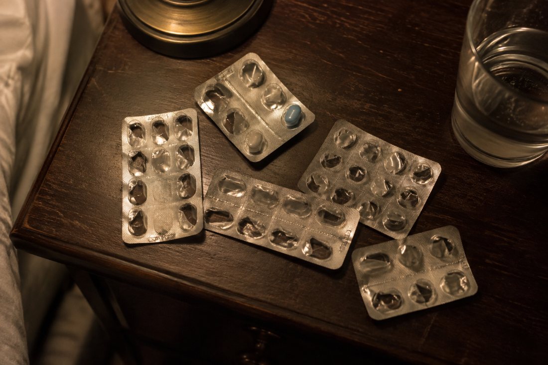 Empty pill blister packs and one last loose tablet on a nightstand at night