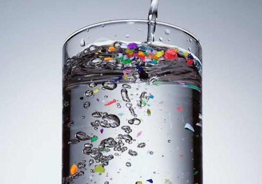 A tall glass of water with colourful microplastic particles floating in it